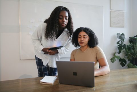 2 African American woman are talking in front of a computer