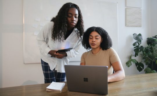 2 African American woman are talking in front of a computer