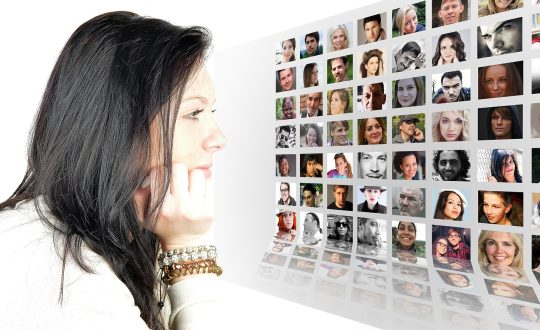 A woman is sitting at a computer looking a pictures of people