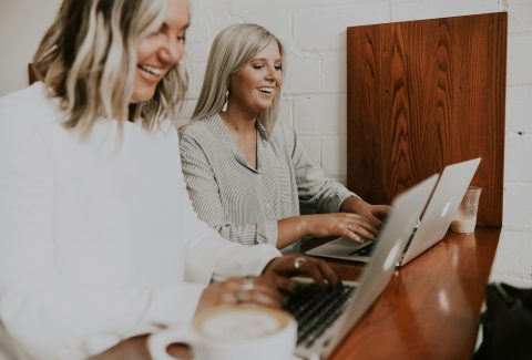 2 Women are sitting at a table typing on their laptop computers