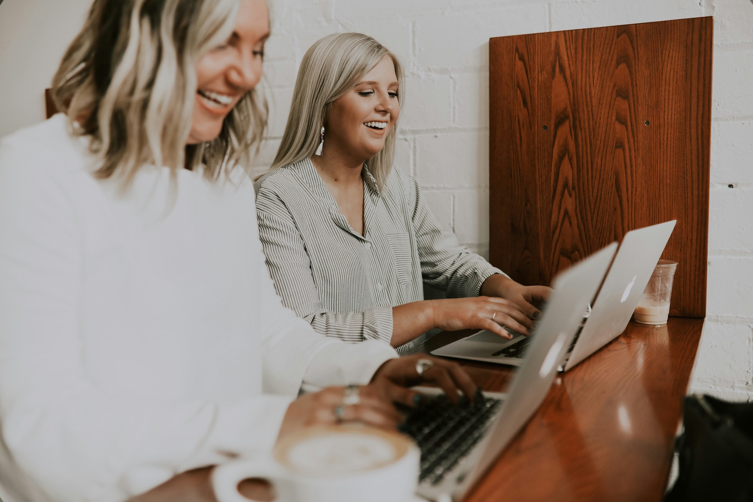 2 Women are sitting at a table typing on their laptop computers