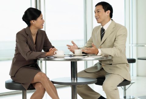 A business man and woman ares sitting at a table and talking