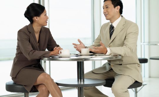 A business man and woman ares sitting at a table and talking