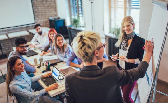 A group of men and woman are sitting around a conference table talking