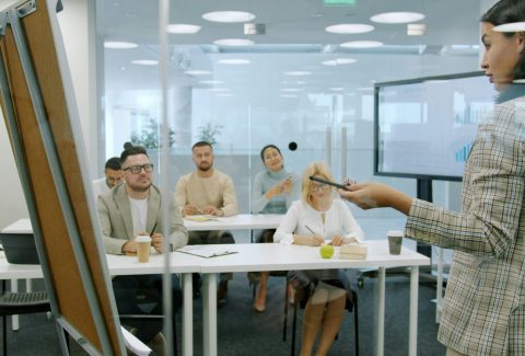A woman is teaching or speaking to a large group of men and woman