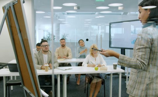 A woman is teaching or speaking to a large group of men and woman