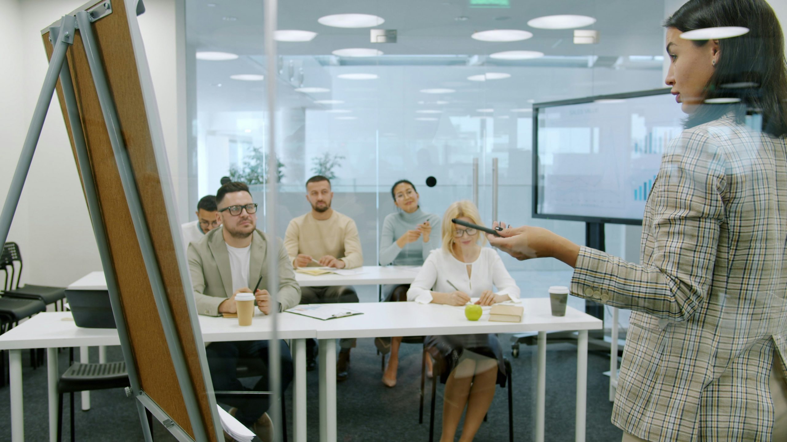 A woman is teaching or speaking to a large group of men and woman
