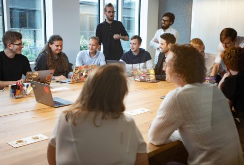 A large group, of men and woman are sitting in a conference room or classroom talking
