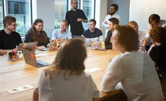 A large group, of men and woman are sitting in a conference room or classroom talking